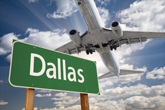 Dallas green road sign and airplane above with dramatic blue sky and clouds