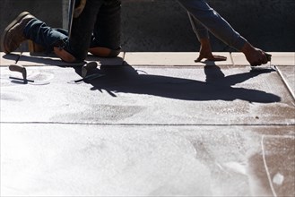 Construction worker smoothing wet cement with hand edger tool