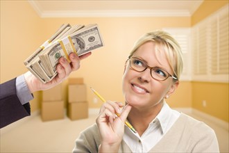 Woman holding pencil being handed stack of money in empty room with boxes