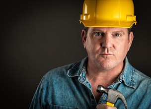 Serious contractor in hard hat holding hammer with dramatic lighting
