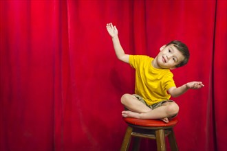 Handsome mixed-race boy sitting on stool in front of red curtain