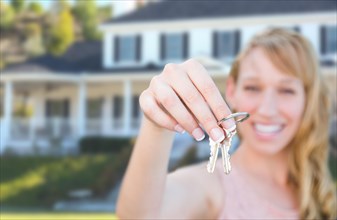 Excited female holding house keys in front of nice new home