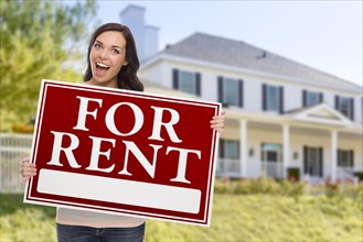 Excited mixed-race female holding for rent sign in front of beautiful house