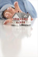 Womans hand reaching for model house on a white surface