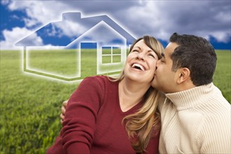 Happy mixed-race couple sitting in grass field with ghosted house behind them