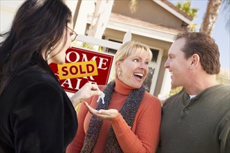 Hispanic female real estate agent handing over new house keys to excited couple