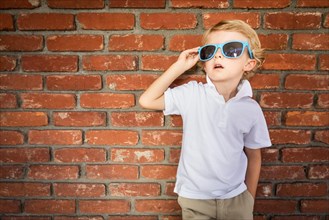 Cute young caucasian boy wearing sunglasses against brick wall