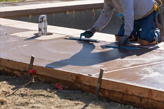 Construction worker smoothing wet cement with trowel tools