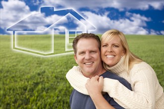 Happy hugging couple in grass field with ghosted house figure behind them