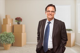 Businessman standing in empty room with packed boxes and plants