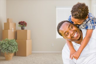 Happy mixed-race african american father and son in room with packed moving boxes