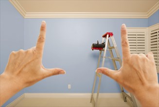 Hands framing blue painted room wall interior with ladder