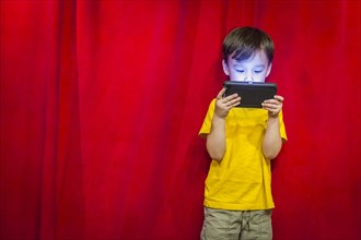 mixed-race boy watching his cell phone in front of red curtain