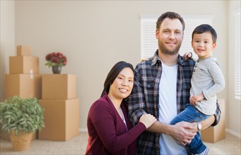 mixed-race chinese and caucasian parents and child inside empty room with moving boxes