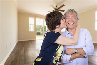 Happy senior chinese couple kissing inside empty room of new house