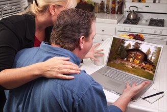 Couple in kitchen using laptop with lake cabin on the screen