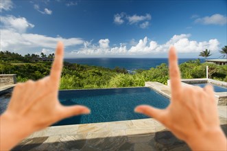 Hands framing pool and hot tub overlooking the ocean