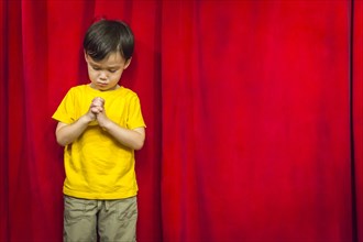 mixed-race boy with praying hands in front of red curtain