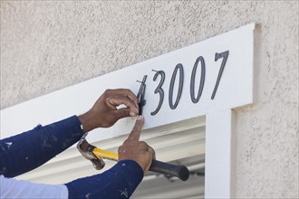 House painter contractor nails address numbers onto house facade