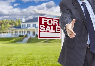 Real estate agent reaches for handshake with sale sign and new house behind