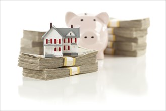 Small house and piggy bank with stacks of hundred dollar bills isolated on a white background