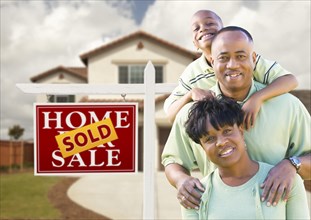 Happy african american family in front of new house and sold real estate sign