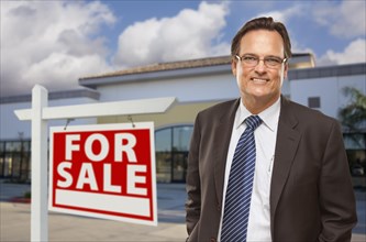 Handsome businessman in front of vacant office building and for sale real estate sign