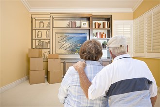 Senior couple in room with moving boxes looking at drawing of entertainment unit