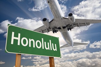 Honolulu green road sign and airplane above with dramatic blue sky and clouds
