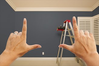 Hands framing grey painted room wall interior with ladder