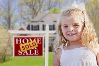 Cute smiling girl in front yard with sold for sale real estate sign and house