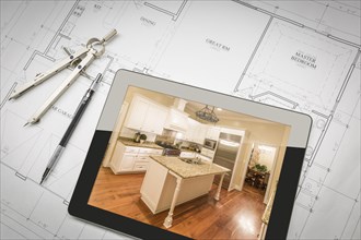 Computer tablet showing finished kitchen sitting on house plans with pencil and compass