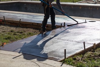 Construction worker smoothing wet cement with trowel tool