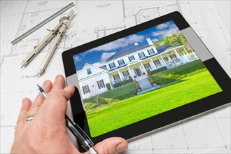 Hand of architect on computer tablet showing home photo over house plans