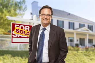 Male real estate agent in front of sold home for sale sign and house