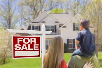 Curious family facing for sale real estate sign and beautiful new house