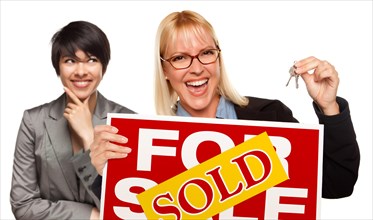 Hispanic female behind with attractive blonde in front holding keys and sold for sale sign isolated on a white background