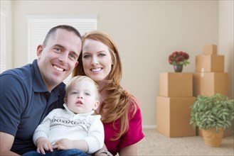 Happy young military family in empty room with packed boxes and plants
