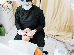 Woman dentist doing endodontics to woman patient.  Dentist with patient lying down. Dentist examining mouth to patient. Dentist performing stomatology