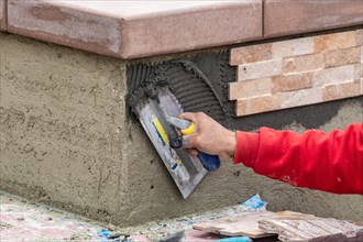 Worker installing wall tile cement with trowel and tile at construction site