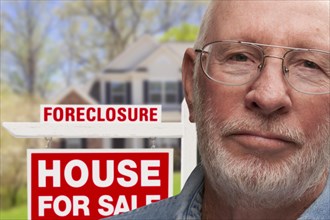 Depressed senior man in front of foreclosure real estate sign and house