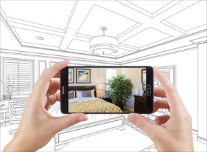 Hands holding smart phone displaying photo of custom bedroom drawing behind