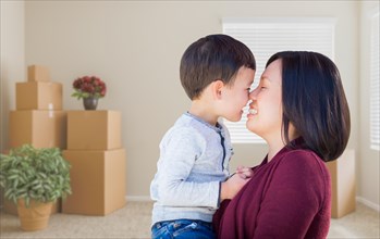 Young mixed-race chinese mother and child in empty room with packed moving boxes and plants