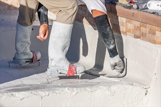 Worker wearing spiked shoes smoothing wet pool plaster with trowel