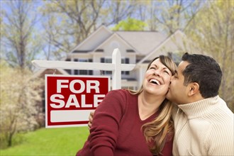 Happy couple in front of for sale real estate sign and new house