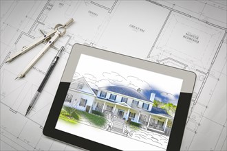 Computer tablet showing house illustration sitting on house plans with pencil and compass