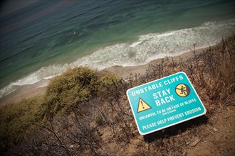 Stay back warning sign on cliff edge near ocean