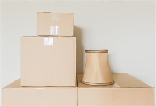 Variety of packed moving boxes and lamp shade in empty room against wall