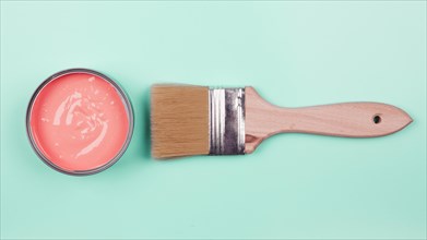 An elevated view of coral paint bucket and paintbrush on mint background