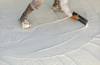 Worker wearing spiked shoes smoothing wet pool plaster with trowel